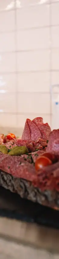 Delizioso e regionale Vassoio di legno rustico con una varietà di salumi affettati, presentato su un tavolo di legno insieme a pane e posate.